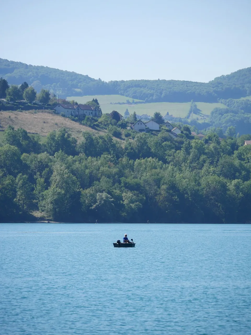 Eau bleue du lac de Paladru, collines boisées et petite embarcation